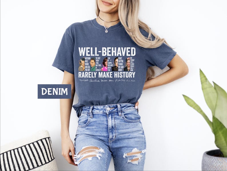 May include: A navy blue t-shirt with a white graphic print that says "Well-Behaved Rarely Make History". The graphic features a collage of famous women and men with quotes about their accomplishments. The shirt is being modeled by a person wearing blue jeans.