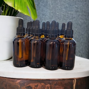 May include: A group of 12 amber glass bottles with black dropper tops. The bottles are arranged in a row on a white surface.