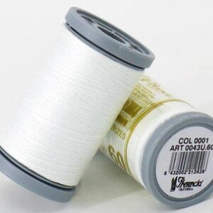 May include: Two spools of white thread with a gray plastic cap. The spool on the right has a label with the text "COL 0001 ART 0043U.60" and a barcode.