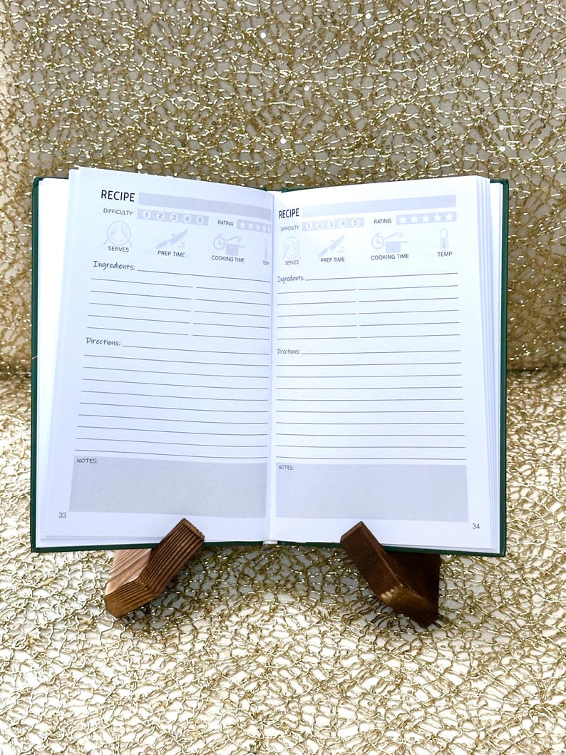May include: An open recipe journal with green covers, displayed on a wooden stand. The pages are white with printed sections for ingredients, directions, and notes. The text "RECIPE" is visible at the top of each page.