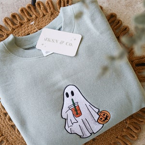 May include: A light green sweatshirt with an embroidered ghost holding a cup of coffee and a small pumpkin. The sweatshirt has a tag that says "JKSN & CO."