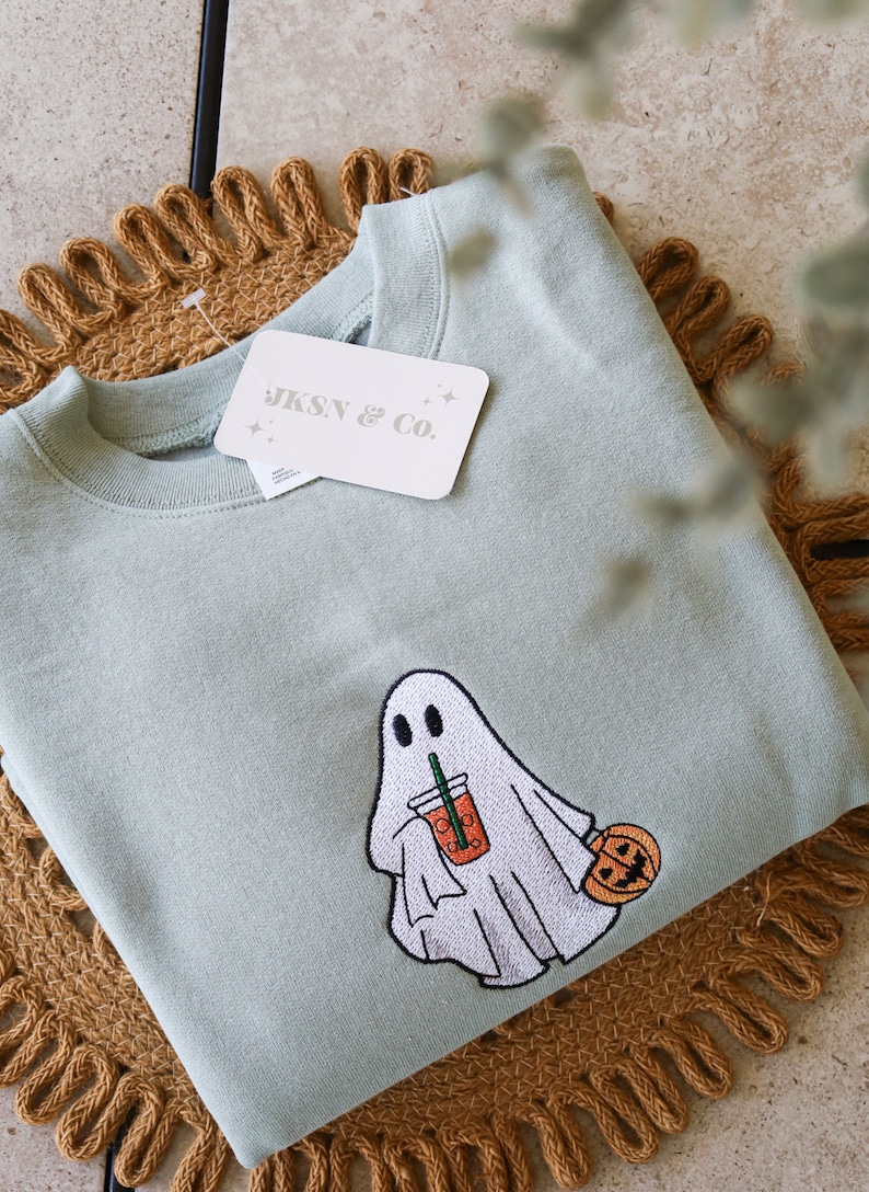 May include: A light green sweatshirt with an embroidered ghost holding a cup of coffee and a small pumpkin. The sweatshirt has a tag that says "JKSN & CO."