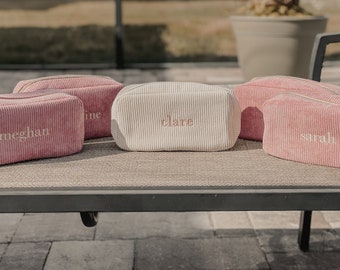 May include: Five pink and white corduroy makeup bags with the names Meghan, Claire, Sarah, and two others embroidered on them.