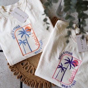 May include: Two white t-shirts with embroidered palm trees and the text "what a crash Florida what a rush".
