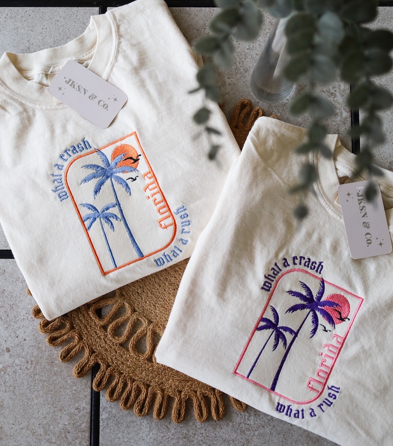 May include: Two white t-shirts with embroidered palm trees and the text "what a crash Florida what a rush".