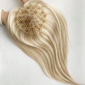 Pode incluir: Uma touca de cabelo loiro com uma base de malha castanho claro. O cabelo é uma mistura de mechas loiras e castanho claro, criando um visual natural e realçado. O cabelo é estilizado em camadas longas e fluidas.