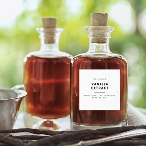 May include: Two glass bottles of homemade vanilla extract with cork stoppers. The bottle on the right has a label that reads "Homemade Vanilla Extract with love, the Johnsons bottled on..."
