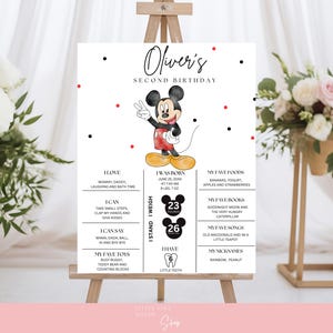 Könnte beinhalten: Ein weißes Schild auf einer Staffelei mit dem Text "Oliver's Second Birthday" und einer Mickey Mouse-Illustration. Das Schild enthält Informationen über den Geburtstag, das Gewicht, die Lieblingsspeisen, Bücher und Spielsachen des Kindes. Rote und schwarze Punkte verzieren die Oberseite.