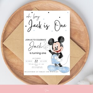 以下が含まれることがあります： ミッキーマウスが描かれた誕生日招待状で、「oh boy Jack is One」というテキストが入っています。招待状には日付、時間、場所の詳細が含まれており、茶色の封筒が入った木製のプレートに置かれています。