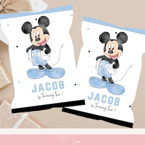 May include: Two white treat bags with a blue top border and a cartoon image of Mickey Mouse. The bags have the text "JACOB is Turning Two!" in blue. Black and gray polka dots are scattered around the bags.