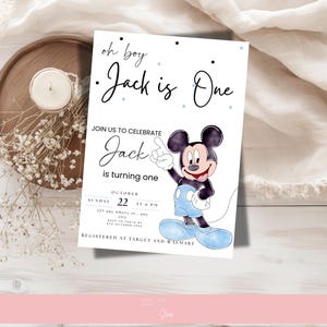 以下が含まれることがあります： ミッキーマウスの誕生日招待状。「oh boy Jack is One」と「Jackの1歳を祝うために参加してください」と書かれています。招待状は青色のアクセントで装飾され、ろうそくと花が置かれた木製のトレイに置かれています。