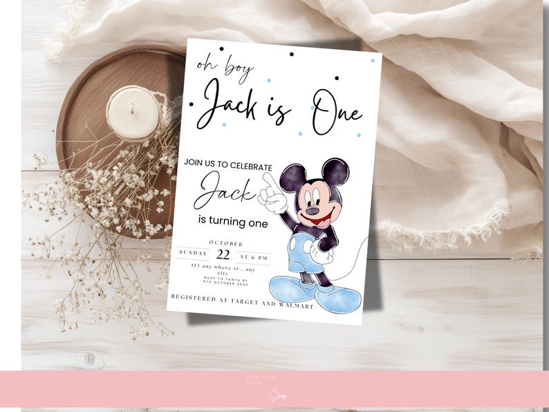 以下が含まれることがあります： ミッキーマウスの誕生日招待状。「oh boy Jack is One」と「Jackの1歳を祝うために参加してください」と書かれています。招待状は青色のアクセントで装飾され、ろうそくと花が置かれた木製のトレイに置かれています。