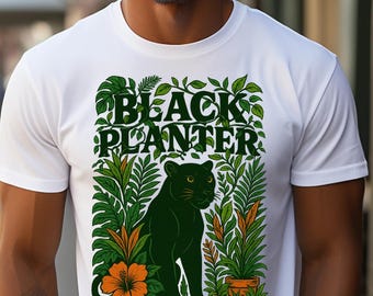 Puede incluir: Camiseta blanca con un gráfico verde y naranja. El gráfico presenta el texto "BLACK PLANTER" sobre una ilustración de pantera verde rodeada de plantas y flores. La camiseta la lleva una persona.