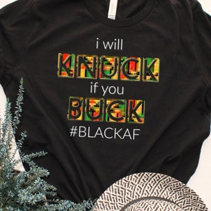 May include: Black t-shirt with the text "i will knock if you buck #BLACKAF" in white. The words "knock" and "buck" are in colorful patterned blocks.