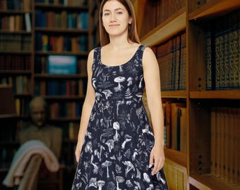 Puede incluir: Un vestido negro sin mangas con un estampado blanco de varios hongos y helechos. El vestido tiene un escote redondo y un corpiño ajustado con una falda acampanada.