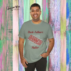 May include: A person wearing a green t-shirt with the text "Black Authors" and a red "Banned" stamp over the list of authors. The text "Matter" is below the list of authors.
