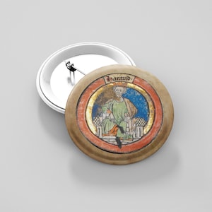 Puede incluir: Un botón redondo con una ilustración medieval de un hombre con túnicas verdes y doradas, sentado en un trono. La ilustración está enmarcada por un borde rojo y dorado, con el nombre "Harald" arriba. El botón está sobre un fondo blanco.
