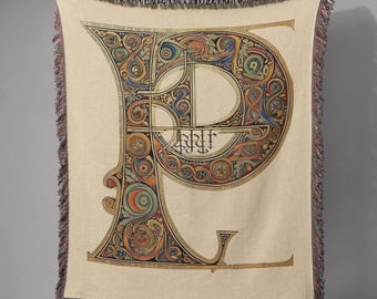May include: Cream-colored throw blanket featuring a large, ornate letter "P" in a colorful, Celtic-inspired design. The letter is filled with intricate patterns in shades of green, blue, red, and gold. The blanket has a fringed edge.