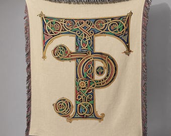 May include: A beige throw blanket featuring a large, ornate letter "P" in a colorful, Celtic knot design. The letter is detailed with red, blue, green, and gold accents. The blanket has a fringed edge.