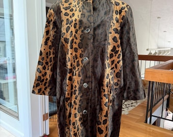 Puede incluir: Un abrigo largo con un estampado de leopardo prominente en tonos marrón, negro y beige. La prenda tiene un cuello alto, mangas largas y un cierre frontal con cinco botones circulares visibles alineados a lo largo del centro.