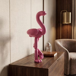May include: A pink flamingo sculpture with a long neck and articulated legs stands on a wooden cabinet. The flamingo has a rounded body and head, with a small, red beak. The sculpture is a decorative item.