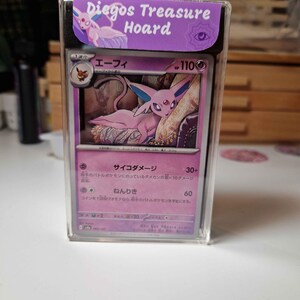 May include: A Pokemon trading card featuring a pink Espeon character, displayed in a clear protective case. The card has Japanese text and a purple border. The case has a purple label that reads "Diegos Treasure Hoard".
