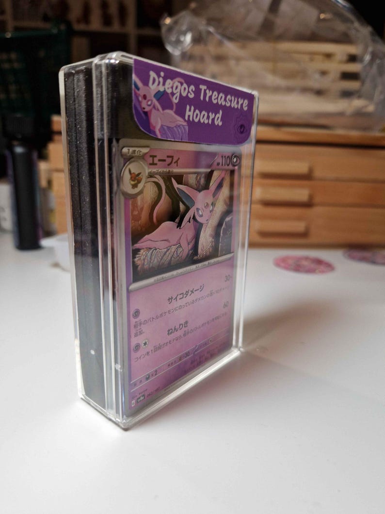 May include: A stack of trading cards in a clear plastic case. The top card features a pink and purple illustration of a creature. The case has a purple label that reads "Diegos Treasure Hoard".