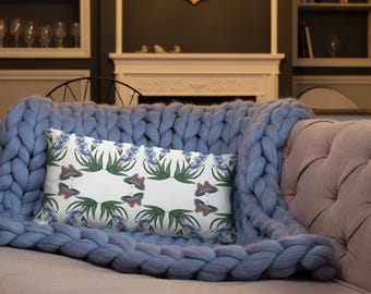 May include: A white throw pillow with a repeating pattern of blue flowers and butterflies. The pillow is on a blue knitted throw blanket.