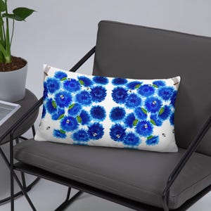 May include: A white lumbar pillow with a blue floral pattern. The flowers are stylized and have a watercolor effect. The pillow is on a gray chair.