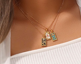May include: Three gold chain necklaces with rectangular pendants featuring colorful enamel designs. The pendants are inspired by tarot cards.