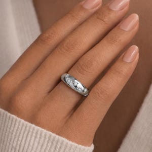 May include: A polished silver-toned band ring featuring a rounded profile and a series of engraved starburst motifs. Each starburst design is centred with a small, clear, sparkling stone, creating a celestial pattern across the metal surface.