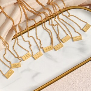 Puede incluir: Un conjunto de collares de oro con colgantes rectangulares que presentan diferentes n&uacute;meros, incluyendo 111, 222, 333, 444, 666, 777, 999 y 1111.