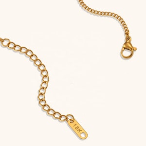 Puede incluir: Un collar de cadena de oro con un cierre de langosta y una etiqueta que dice "18K".