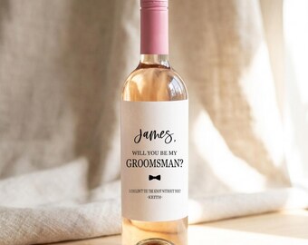 May include: A clear glass bottle filled with a light pink liquid, topped with a solid pink cap. The white label features the text: James, WILL YOU BE MY GROOMSMAN? with a small black bow tie icon and the text: I COULDN'T TIE THE KNOT WITHOUT YOU? -KEITH-