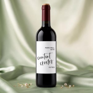 May include: A dark glass wine bottle with a white rectangular label featuring the black text PAIRS WELL WITH content creator DUTIES. The bottle has a dark red neck and a light brown cork stopper, standing upright with a smooth, cylindrical body shape.