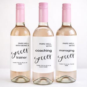 May include: Three wine bottles with pink tops and white labels. The labels read "Pairs Well With Being a Soccer Trainer", "Pairs Well With Coaching Soccer", and "Pairs Well With Managing Soccer". Each label includes a thank you message.