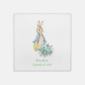 Puede incluir: Una ilustración de acuarela de un conejo marrón con una chaqueta azul y sosteniendo un pollito amarillo. El conejo está de pie junto a un ramo de flores azules y blancas. El texto "Baby Maida September 21, 2024" está escrito debajo de la ilustración.