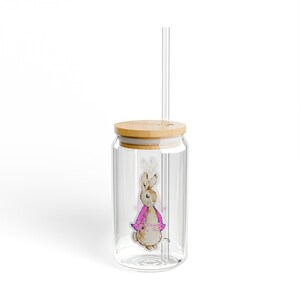 May include: A clear glass drinking glass with a bamboo lid and a straw. The glass has a sticker of a rabbit wearing a pink jacket. The sticker says "The Adventures of Peter Rabbit".