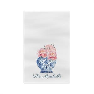 May include: White kitchen towel with a blue and white porcelain vase with pink peonies and the text "The Marshalls" in blue.