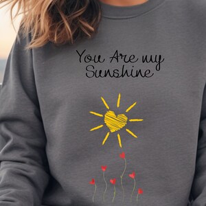 May include: Gray sweatshirt with the text "You Are my Sunshine" in black script. A yellow sun with a heart in the center and red hearts on stems are below the text.