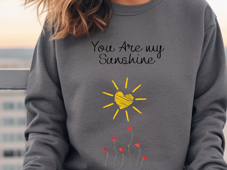 May include: Gray sweatshirt with the text "You Are my Sunshine" in black script. A yellow sun with a heart in the center and red hearts on stems are below the text.