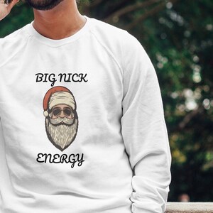Può includere: Felpa bianca a maniche lunghe con una grafica di Babbo Natale con occhiali da sole e il testo "BIG NICK ENERGY".