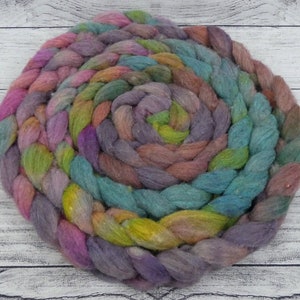 May include: A colorful hand-spun yarn in shades of purple, pink, green, and blue, arranged in a spiral.