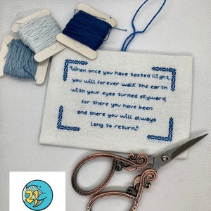 Puede incluir: Un bordado de punto de cruz blanco con hilo azul, que presenta una cita sobre la sensación de volar. La cita dice: "Cuando hayas probado el vuelo, caminarás para siempre por la tierra con los ojos puestos en el cielo, porque has estado allí y siempre anhelarás volver." El bordado está acompañado por un pequeño par de tijeras adornadas y un logotipo de 21 Whales.