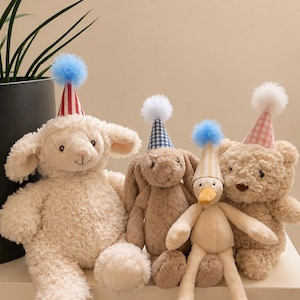 May include: A collection of four plush toys including a cream lamb, a brown bunny, a light yellow duck, and a tan bear. Each toy wears a small, pointed party hat with a fluffy pom-pom on top. The hats feature red stripes, blue gingham, yellow stripes, and pink gingham patterns.