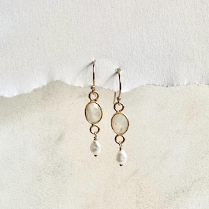 May include: A pair of gold earrings with white oval-shaped stones and a single white pearl dangling from each earring.