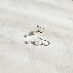 May include: A pair of gold earrings with a white oval gemstone and a small white pearl dangle.