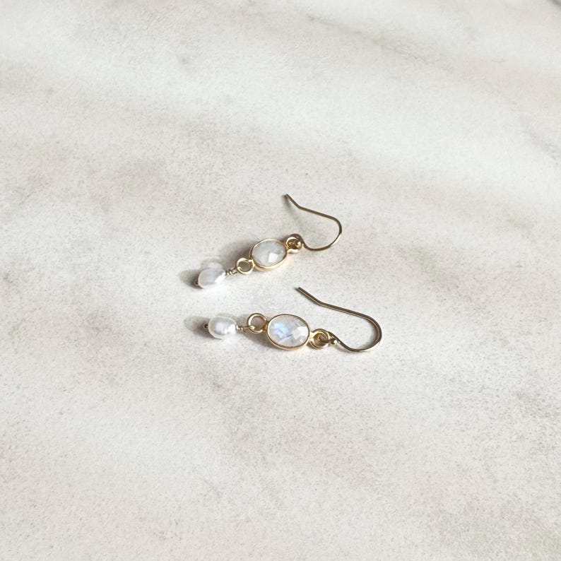May include: A pair of gold earrings with a white oval gemstone and a small white pearl dangle.
