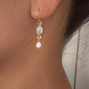 May include: A pair of gold earrings with a white moonstone and a white pearl dangle. The earrings are simple and elegant.