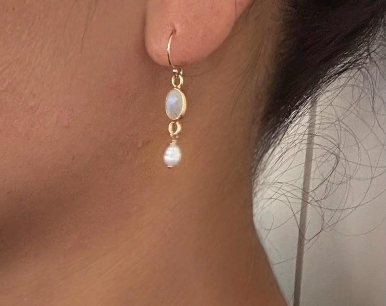 May include: A pair of gold earrings with a white moonstone and a white pearl dangle. The earrings are simple and elegant.